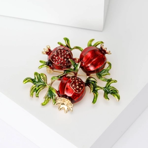 Detailed close-up of a red enamel pomegranate brooch with green leaves and golden seeds