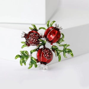 Macro detail of enamel red pomegranate brooch with intricate green leaves and seeds