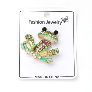 Detail shot of vintage frog brooch with green rhinestones and enamel on white card