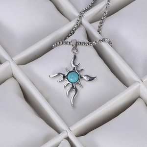 Detailed macro view of a silver flame cross pendant with blue stone on a box chain