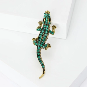 Lizard brooch in antique gold with green crystals on minimalist geometric white podium
