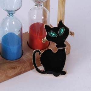 Detail van een zwarte emaille kattenbroche met groene ogen naast een houten zandloper