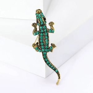 Detailed close-up of a gold-toned lizard brooch with green rhinestones on white geometric blocks
