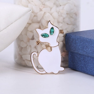 Detail van witte emaille kattenbroche met groene edelstenen ogen en goudaccenten