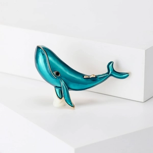 Artistic blue enamel whale brooch with gold-plated edges on a white geometric stand