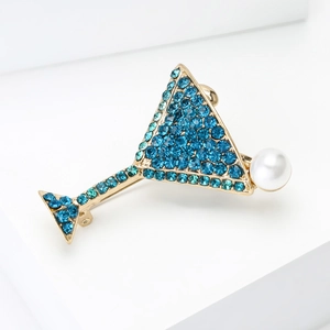 Détail de l'élégante broche verre à cocktail dorée avec strass bleus et perle blanche