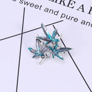 Detail of maple leaf brooch featuring blue-purple gradient enamel and three white pearls