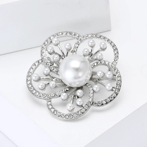 Elegant silver flower brooch with large pearl and white rhinestones on a white pedestal