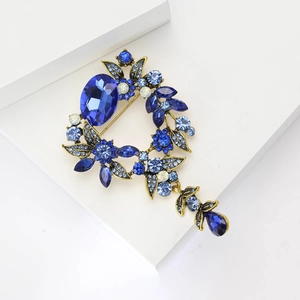 Vue détaillée de la broche à fleurs et pompons avec cristaux bleus sur base dorée