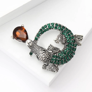 Dettaglio spilla a coccodrillo vintage con strass verdi e gemma color ambra