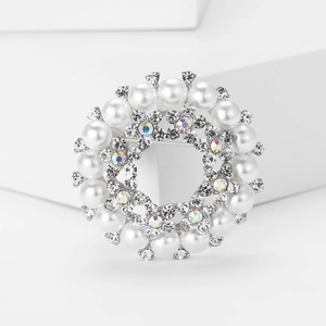 Dettaglio di una spilla argentata con perle bianche e strass scintillanti incastonati
