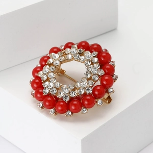 Dettaglio macro di spilla rotonda vintage con perle rosse, strass e base in lega dorata