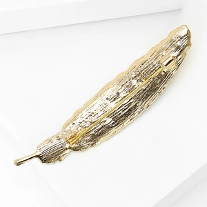 Detail showing the back of a golden feather brooch with a metal pin fastening mechanism