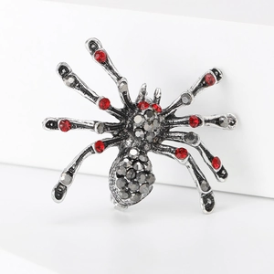 Silver spider brooch with red and grey rhinestones on a minimalist white stage