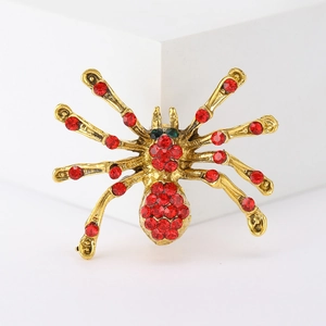 Macro detail of a golden spider brooch featuring vibrant red rhinestones and green eyes