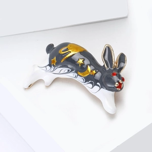 Vue détaillée d'une broche lapin en émail noir et blanc avec motifs dorés de lune et d'étoiles