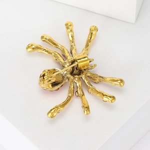Back view of gold spider brooch with safety pin clasp and red rhinestone details