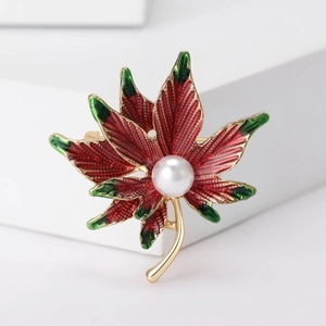 Close-up of red and green enamel maple leaf brooch with white pearl on gold base
