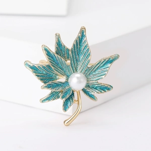 Detail of maple leaf brooch with blue glitter enamel and white pearl accent