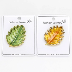 Detailed macro view of two crystal leaf brooches on a white display card with rhinestones