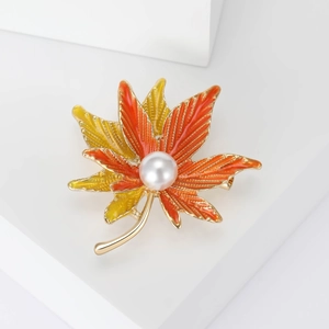 Detail of maple leaf brooch with orange enamel gradient, pearl accent and gold metal frame