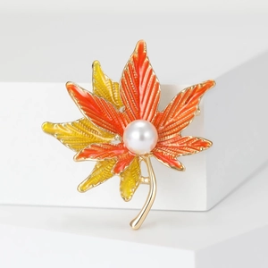 Close-up of maple leaf brooch with orange enamel gradient and a white pearl accent