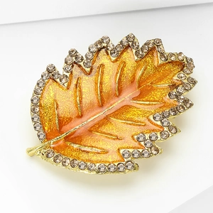 Detailed close-up of leaf brooch with orange enamel, gold plating and crystals