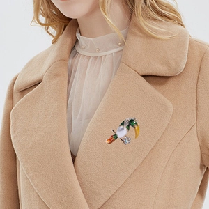 Green enamel toucan brooch with large pearl and small rhinestone on a camel wool coat