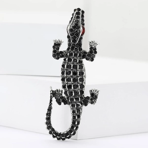 Detailed close-up of a crocodile brooch with black rhinestones on a white podium