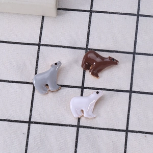 Three cute enamel polar bear brooches in grey, brown, and white on a checkered fabric background