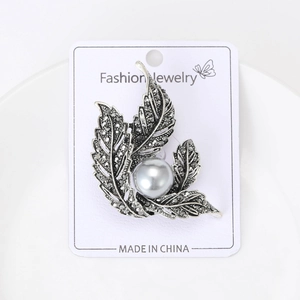 Macro detail of retro leaf brooch featuring a grey pearl and dark stones on display card