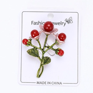 Detail of handcrafted cherry brooch with red pearls and green enamel on a display card