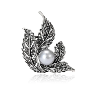 Vintage leaf brooch with dark crystals and a centered silver pearl on white background