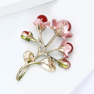 Floral brooch with pink enamel petals and red pearl accents on a gold base