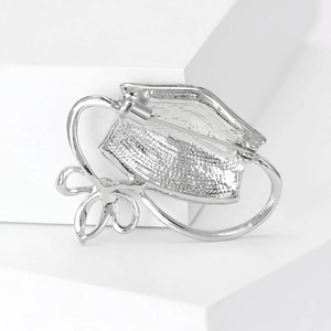 Minimalist silver enamel mask brooch with sleek bow design and hammered metal texture