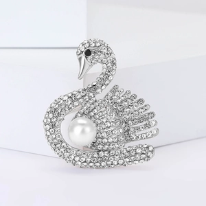 Élégante broche cygne argentée avec cristaux et perle blanche sur un piédestal