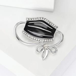 Detailed close-up of a silver face mask brooch with black enamel and sparkling rhinestones