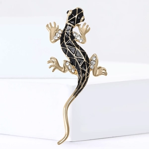 Broche gecko dorée avec émail noir et strass blancs sur un socle blanc minimaliste