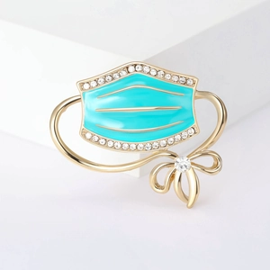 Detail of teal enamel face mask brooch with gold bow and sparkling crystal rhinestones