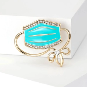Tiffany blue enamel face mask brooch with gold trim and rhinestones on a white background