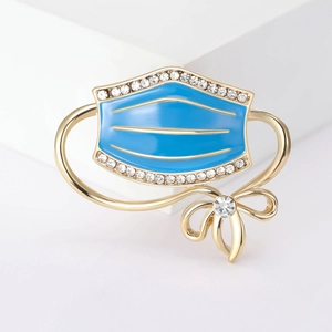 Detailed close-up of a blue enamel mask brooch with rhinestones and a gold bow detail