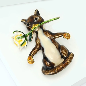 Détail d'une broche chat en émail brun tenant une fleur avec des strass verts brillants