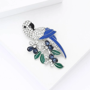 Vibrant parrot and flower brooch with blue rhinestones and green enamel on a white stand