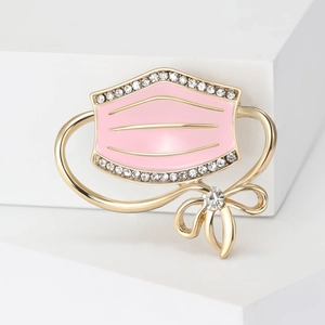 Detail of pink enamel mask brooch with gold edges and sparkling rhinestones