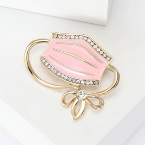 Detailed close-up of pink enamel face mask brooch with golden bow and crystals