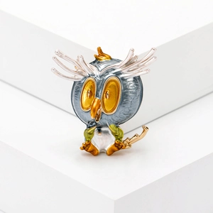 Detail of owl brooch featuring blue enamel finish and vibrant yellow eyes on metal base
