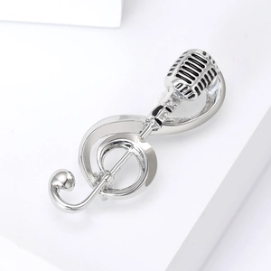 Close-up of silver musical treble clef and microphone brooch with black enamel detail