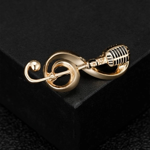 Macro shot of gold treble clef and microphone brooch with black enamel details