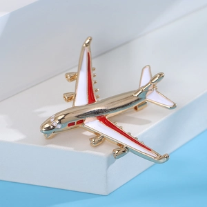Detailed close-up of a gold aircraft brooch with elegant white and red enamel finish