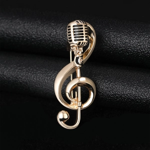 Detailed macro view of golden treble clef and microphone brooch on black leather background